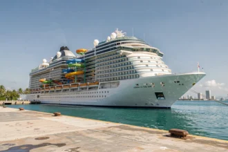 Vue grand angle d'un immense paquebot de croisière moderne dans un port caribéen avec toboggans colorés et parc aquatique visible sur les ponts supérieurs