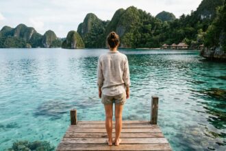 Voyageuse sur un ponton en bois surplombant les eaux turquoise de Raja Ampat avec des îles karstiques en arrière-plan