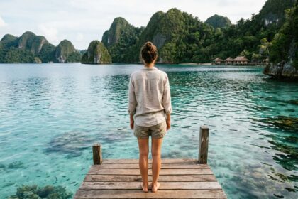 Voyageuse sur un ponton en bois surplombant les eaux turquoise de Raja Ampat avec des îles karstiques en arrière-plan